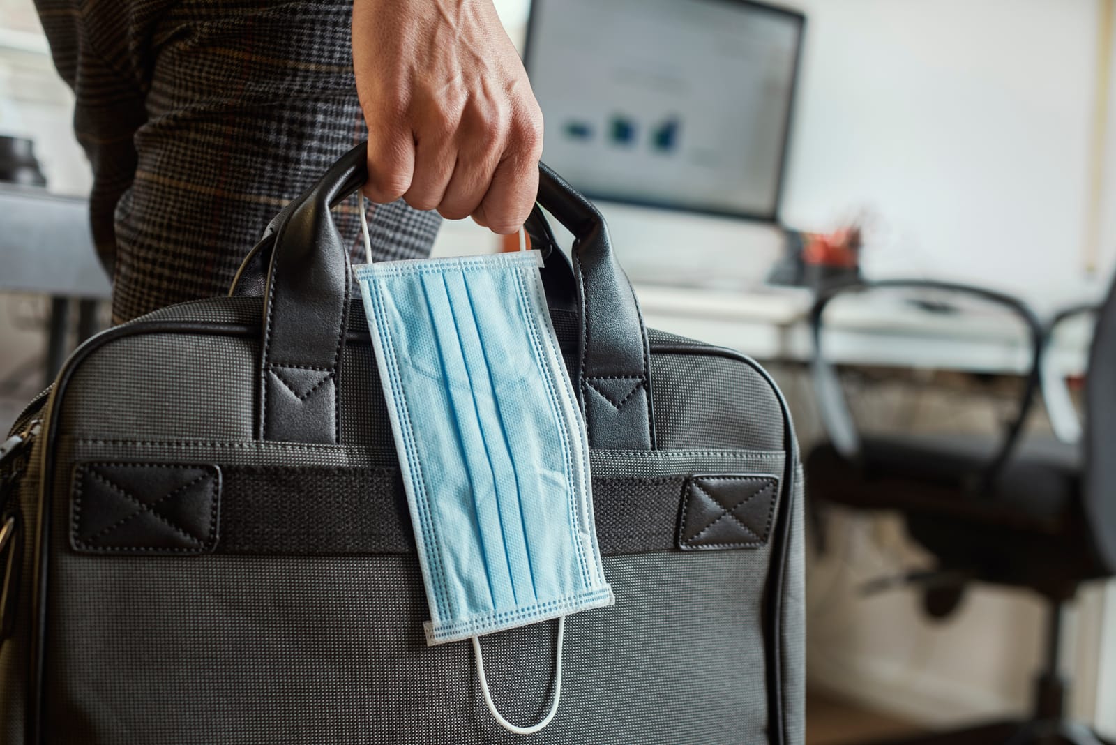 Man in office holding briefcase and surgical mask